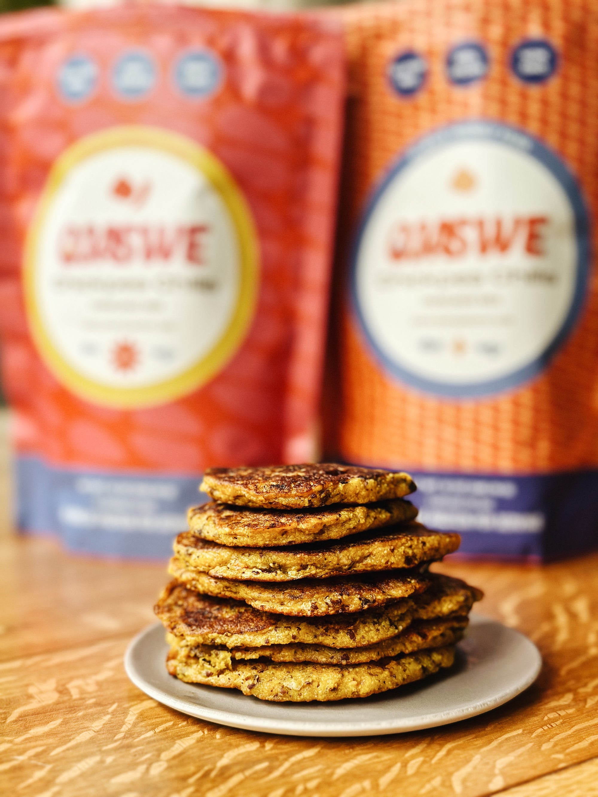 Image shows chilla mix bags in blur in the back and a plate of stacked pancakes in the foreground.